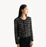 Black female tweed jacket with crewneck, four front pockets, velvet metal logo buttons, and buttoned sleeve vents. 