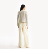 White female tweed jacket with crewneck, four front pockets, velvet metal logo buttons, and buttoned sleeve vents. rear-view.