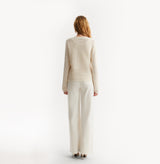 Woman wearing a beige sweater and white pants on a white background, rear-view