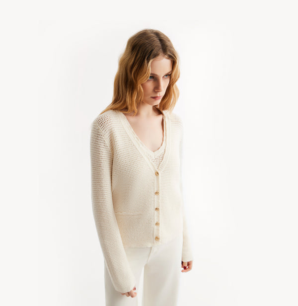 Woman wearing a cream-colored cardigan over a white top on a white background, left-view