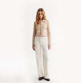 Woman wearing a beige vest over a brown top and white pants on a white background, front-view