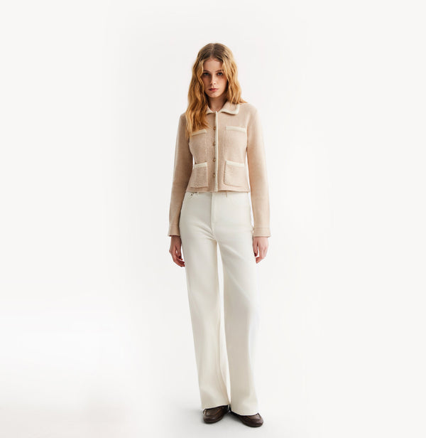 Woman wearing a beige vest over a brown top and white pants on a white background, front-view