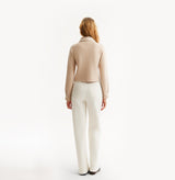 Woman wearing a beige vest over a brown top and white pants on a white background, rear-view