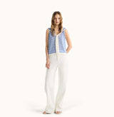 Woman wearing a blue and white striped sleeveless top with a white outfit on a white background, front-view